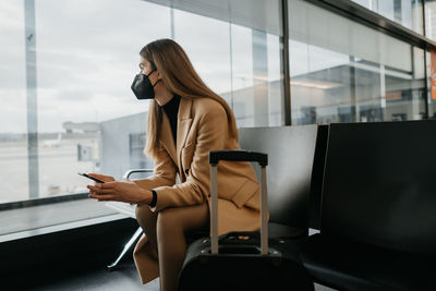 Side view of woman using mobile phone while sitting at airport