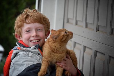 Portrait of happy boy with cat standing by door