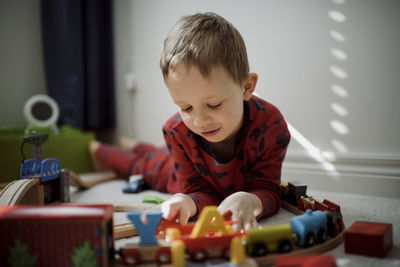 Cute boy playing with model train set while lying on carpet at home