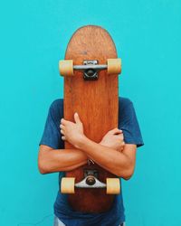 Man holding skateboard against turquoise wall