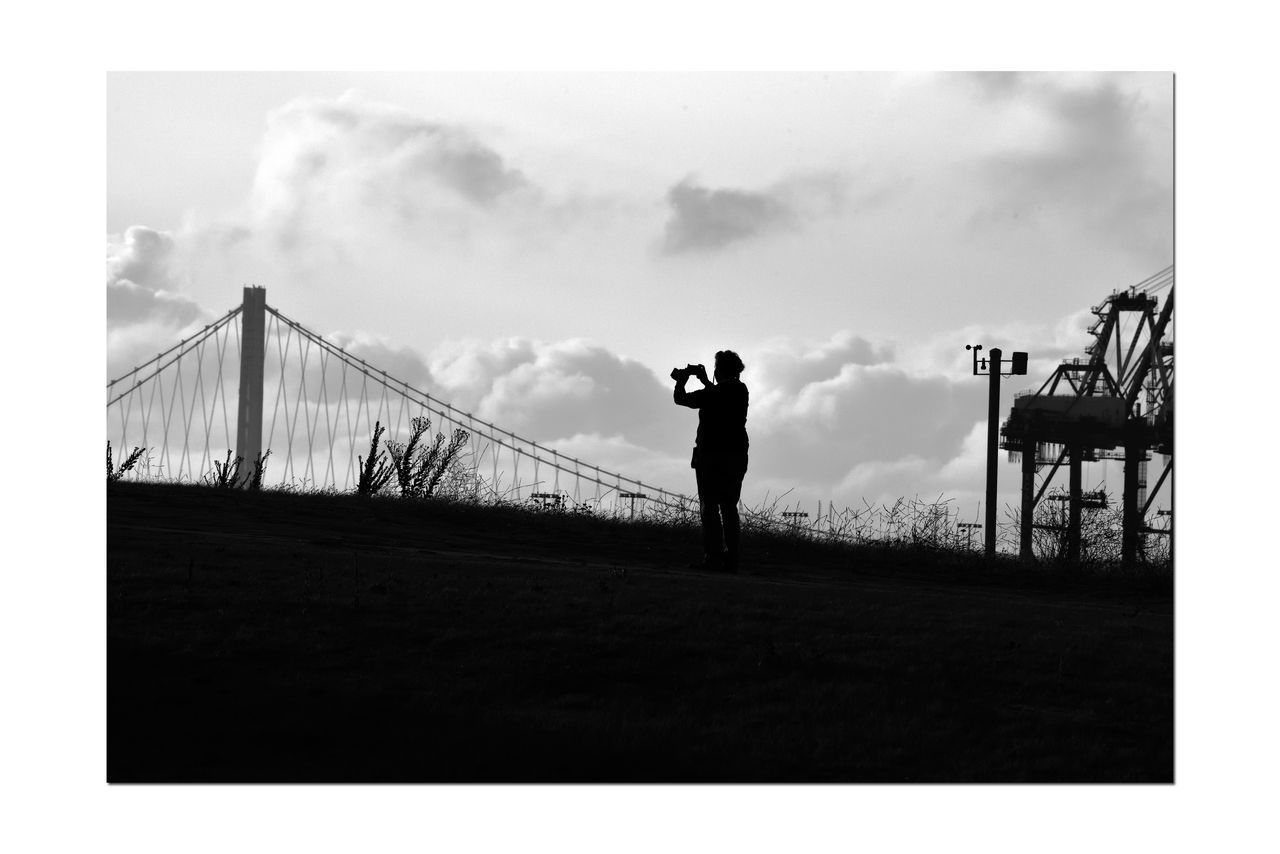 SILHOUETTE MAN PHOTOGRAPHING BY BRIDGE AGAINST SKY