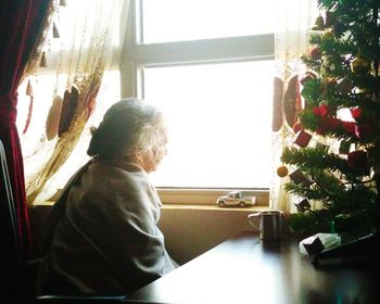 Side view of senior woman sitting by christmas tree on table at home