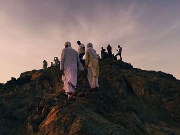 People walking on rocks against sky during sunset