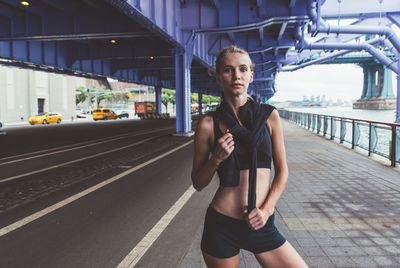 Portrait of woman standing on footpath by road