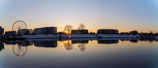 Reflection of buildings in lake against sky at sunset