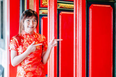 Portrait of smiling woman standing against red wall