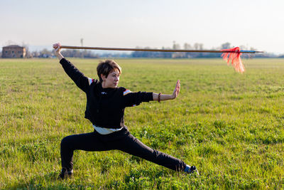 Caucasian young woman practicing wushu martial art on a green meadow with a long spear