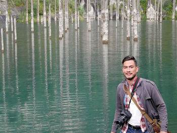 Man with a camera and messenger bag looks into the camera in front of lake kaindy, kazakhstan