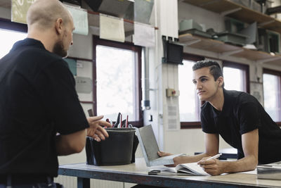 Young male teacher explaining to student in workshop