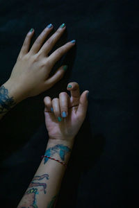 Cropped hands of woman with blue nail polish and tattoo over black background