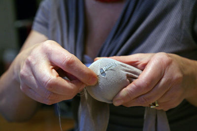 Midsection of woman stitching sock at home
