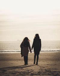 Rear view of friends standing on beach against sky