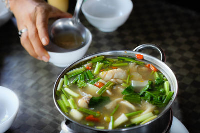 High angle view of cropped hand serving soup in bowl on table