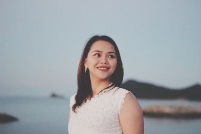 Thoughtful young woman standing at beach against clear sky