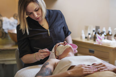 Beautician applying face mask to woman in spa