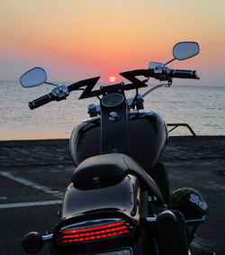 Close-up of bicycle by sea against sky during sunset