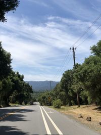 Road by electricity pylon against sky