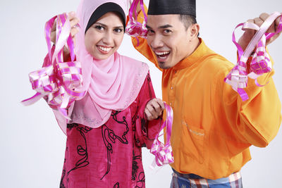 Portrait of happy couple in traditional clothing holding decorations against white background