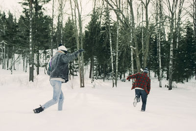 Playful friends running by trees on snow covered landscape
