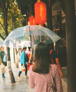 Rear view of woman walking with umbrella on sidewalk during monsoon