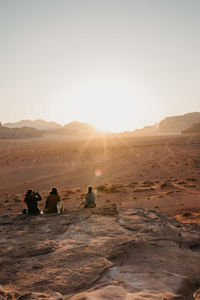 People sitting on sand at desert against clear sky