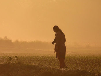 Full length of woman standing on field against sky during sunrise 