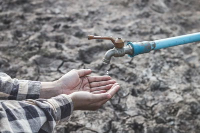 Cropped image of hands catching water drop falling from faucet during drought