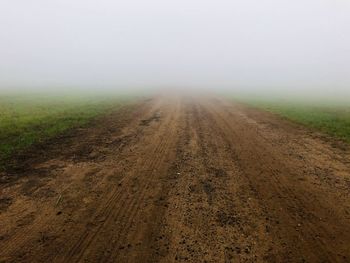 Dirt road amidst field against sky