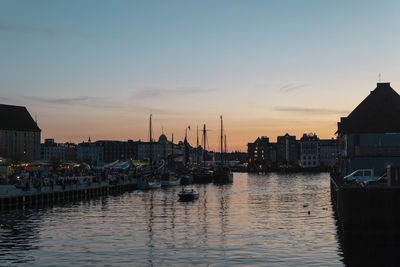 Sailboats moored in river against buildings in city at sunset