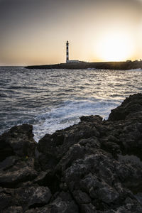 Lighthouse by sea against sky during sunset