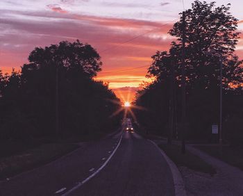 Road amidst silhouette trees against sky during sunset