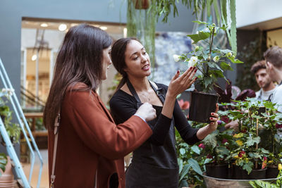Female owners showing flower plant to mid adult customers at store