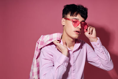 Young man wearing sunglasses against pink background