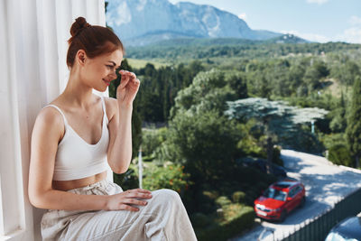 Young woman looking away while sitting on car