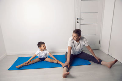 Grandmother and her grandson are sitting on a yoga mat in a white apartment at home