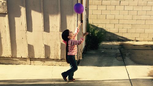 Side view full length of girl playing with balloon on footpath