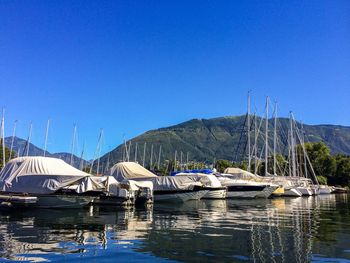 Boats moored in lake against clear blue sky