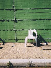 Broken chair by green wall on sunny day