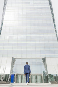 Businessman holding laptop and skateboard walking towards office building