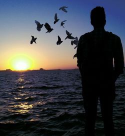 Silhouette of man flying over sea during sunset