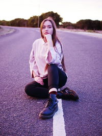 Portrait of beautiful young woman sitting on road against sky