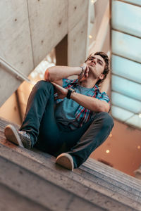 Low angle view of young man looking away while sitting on staircase