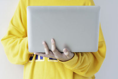 Close-up of boy holding yellow paper over white background