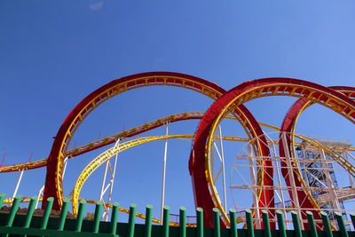 Low angle view of rollercoaster against clear blue sky