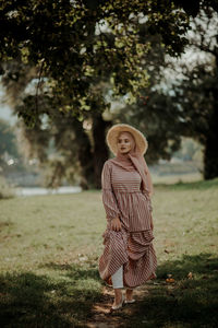 Portrait of woman standing by tree on field