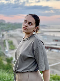 Portrait of young woman standing against lake during sunset