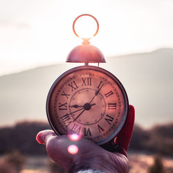 Close-up of hand holding clock against sky