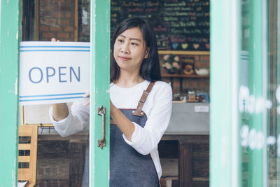 Female owner putting open sign on door in cafe