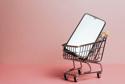 Close-up of shopping cart against yellow background