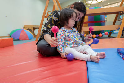 Cute girl with teacher playing on carpet in kindergarten